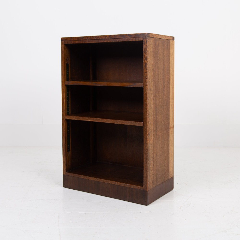A 1930s dark oak open bookcase featuring two adjustable shelves, a leather-inset top surface, and a solid plinth base.