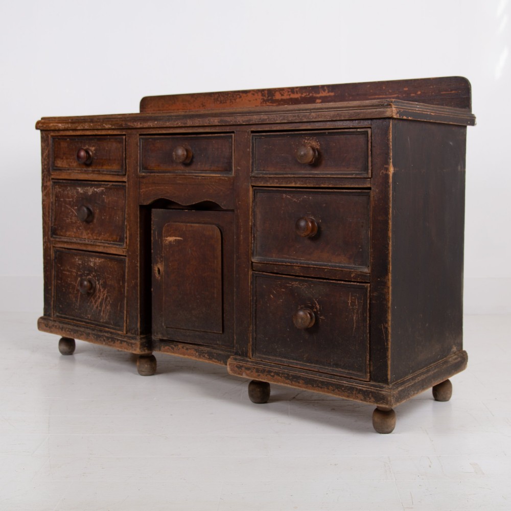 A 19th-century dark brown painted wooden kitchen dresser with seven drawers, a central cupboard, wooden knobs, and turned feet. View II