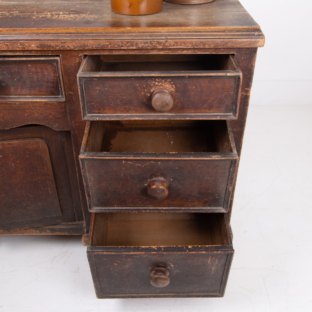 A 19th-century dark brown painted wooden kitchen dresser with seven drawers, a central cupboard, wooden knobs, and turned feet. View VI