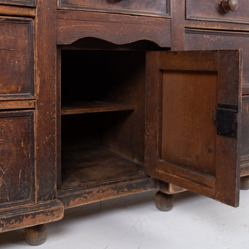 A 19th-century dark brown painted wooden kitchen dresser with seven drawers, a central cupboard, wooden knobs, and turned feet. View X