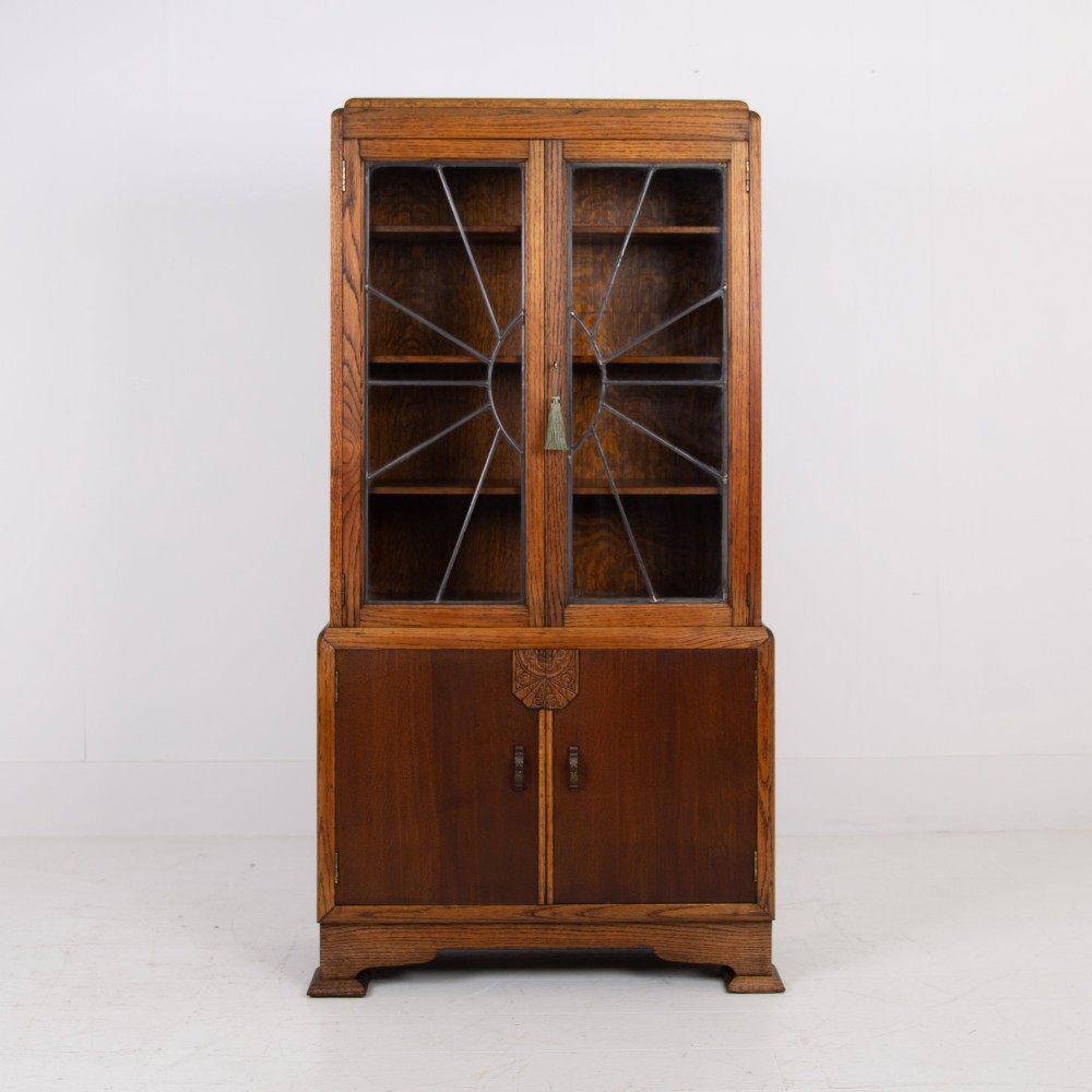 An Art Deco oak cabinet featuring two upper leaded glass doors with a geometric motif and a lower two-door wooden cupboard on stepped feet. View II