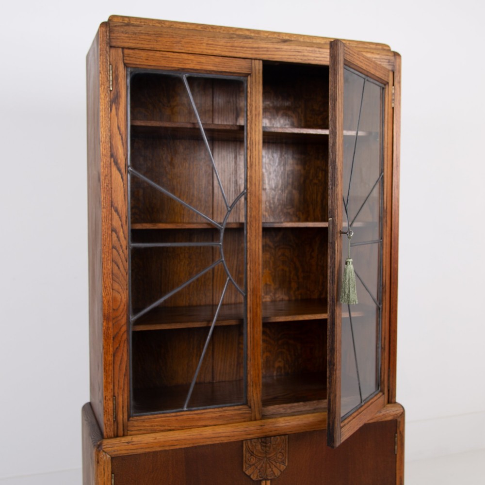 An Art Deco oak cabinet featuring two upper leaded glass doors with a geometric motif and a lower two-door wooden cupboard on stepped feet. View IV