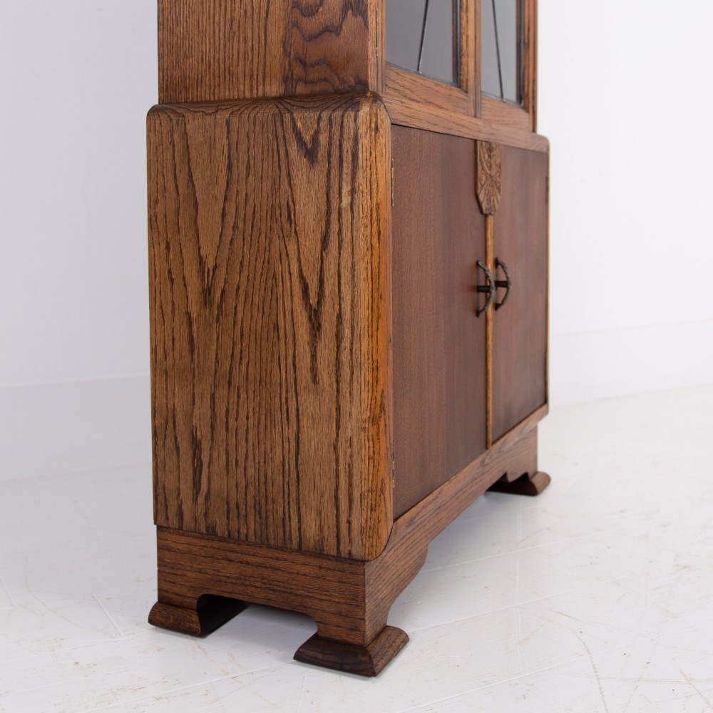 An Art Deco oak cabinet featuring two upper leaded glass doors with a geometric motif and a lower two-door wooden cupboard on stepped feet. View V