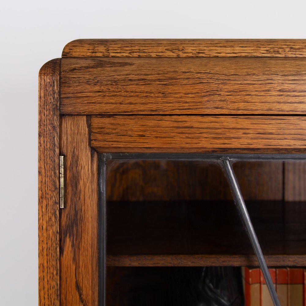 An Art Deco oak cabinet featuring two upper leaded glass doors with a geometric motif and a lower two-door wooden cupboard on stepped feet. View VI