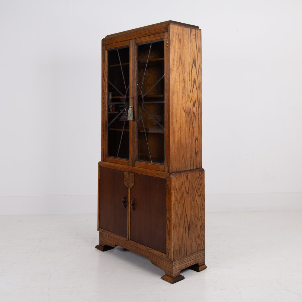 An Art Deco oak cabinet featuring two upper leaded glass doors with a geometric motif and a lower two-door wooden cupboard on stepped feet. View VII