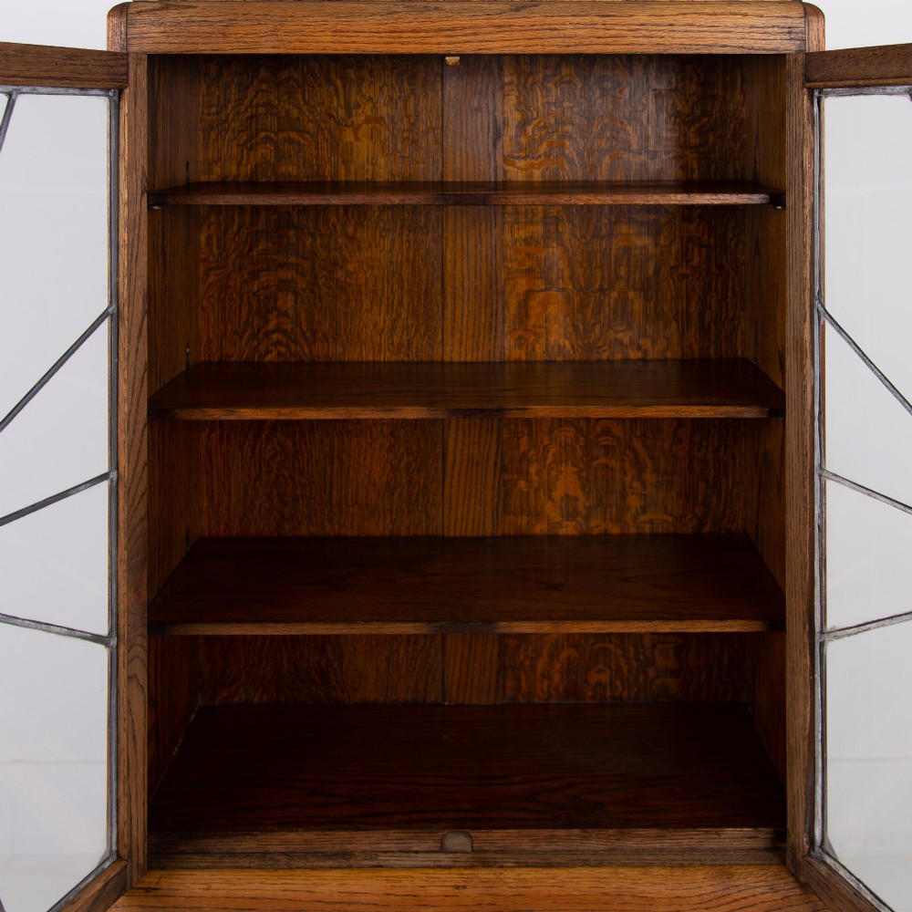 An Art Deco oak cabinet featuring two upper leaded glass doors with a geometric motif and a lower two-door wooden cupboard on stepped feet. View X