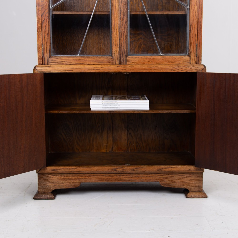 An Art Deco oak cabinet featuring two upper leaded glass doors with a geometric motif and a lower two-door wooden cupboard on stepped feet. View XI