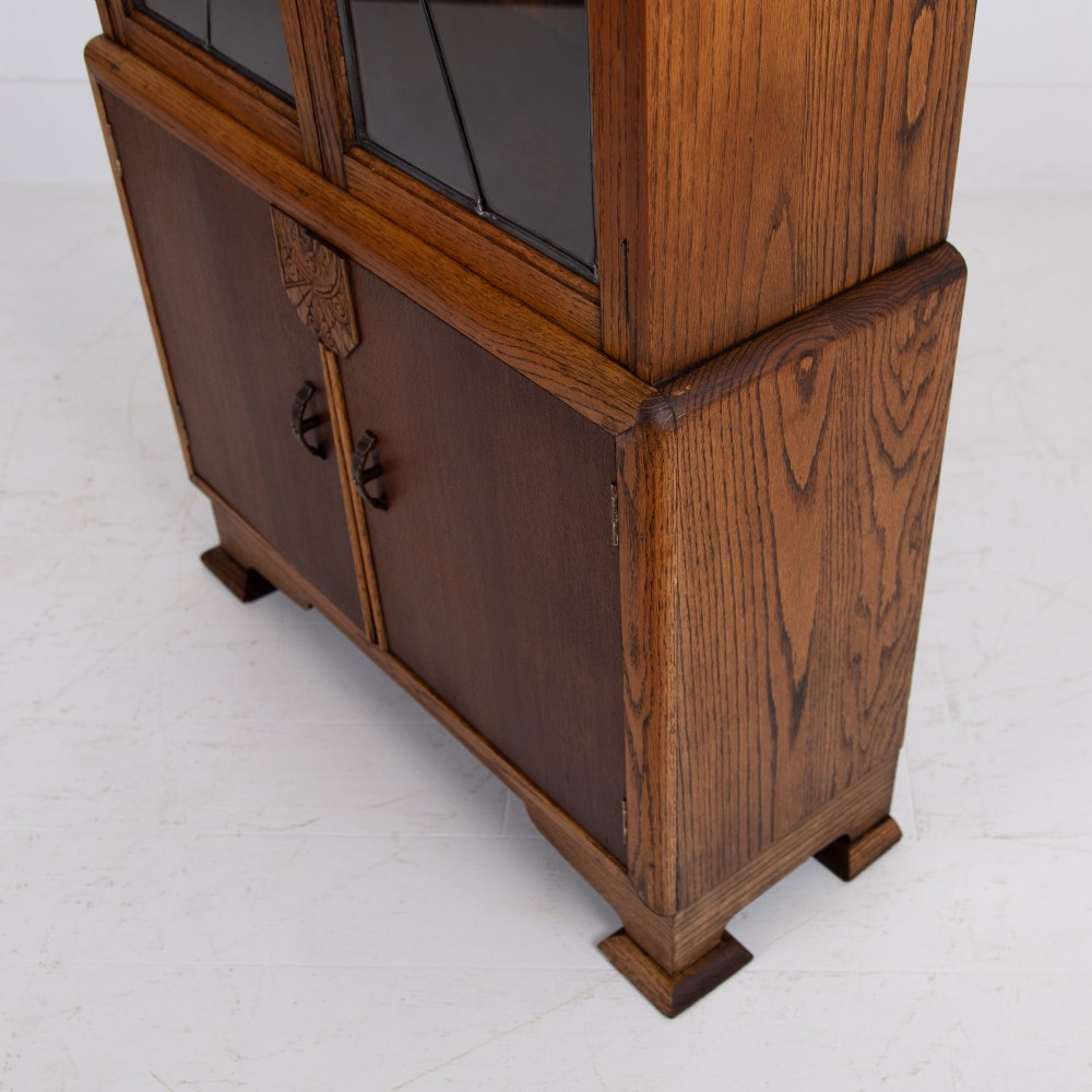 An Art Deco oak cabinet featuring two upper leaded glass doors with a geometric motif and a lower two-door wooden cupboard on stepped feet. View XIII