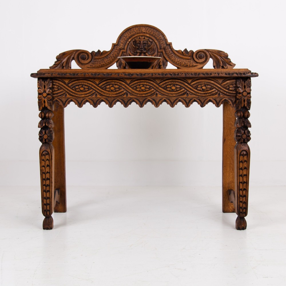 An ornate carved oak console table with a decorative mask crest upstand, an intricate interlace apron design, and carved turned legs.