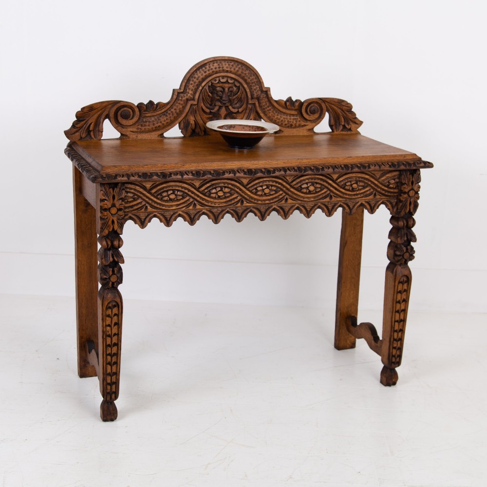 An ornate carved oak console table with a decorative mask crest upstand, an intricate interlace apron design, and carved turned legs. View II