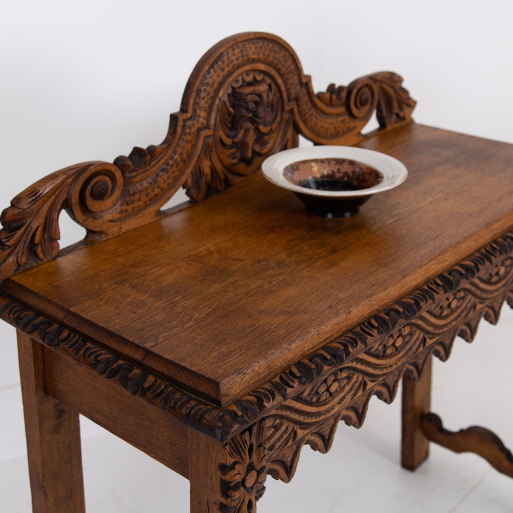 An ornate carved oak console table with a decorative mask crest upstand, an intricate interlace apron design, and carved turned legs. View III