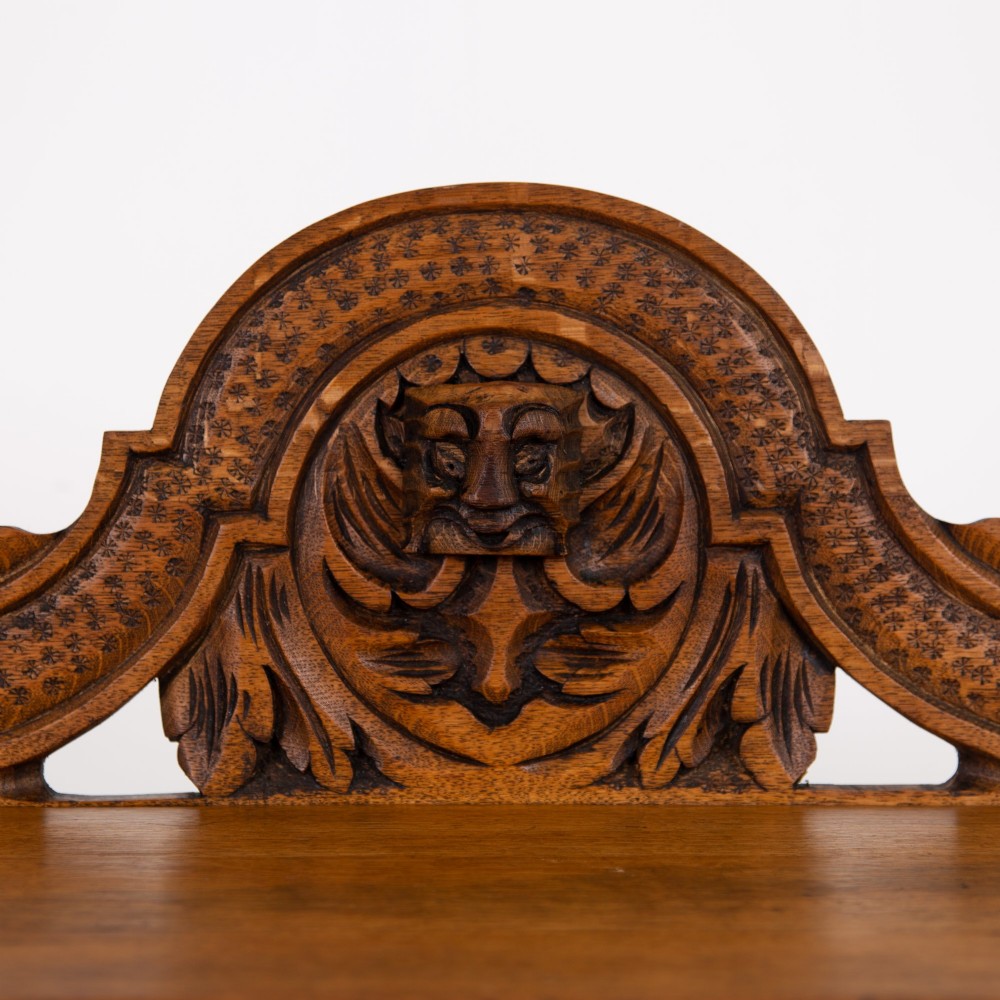 An ornate carved oak console table with a decorative mask crest upstand, an intricate interlace apron design, and carved turned legs. View V