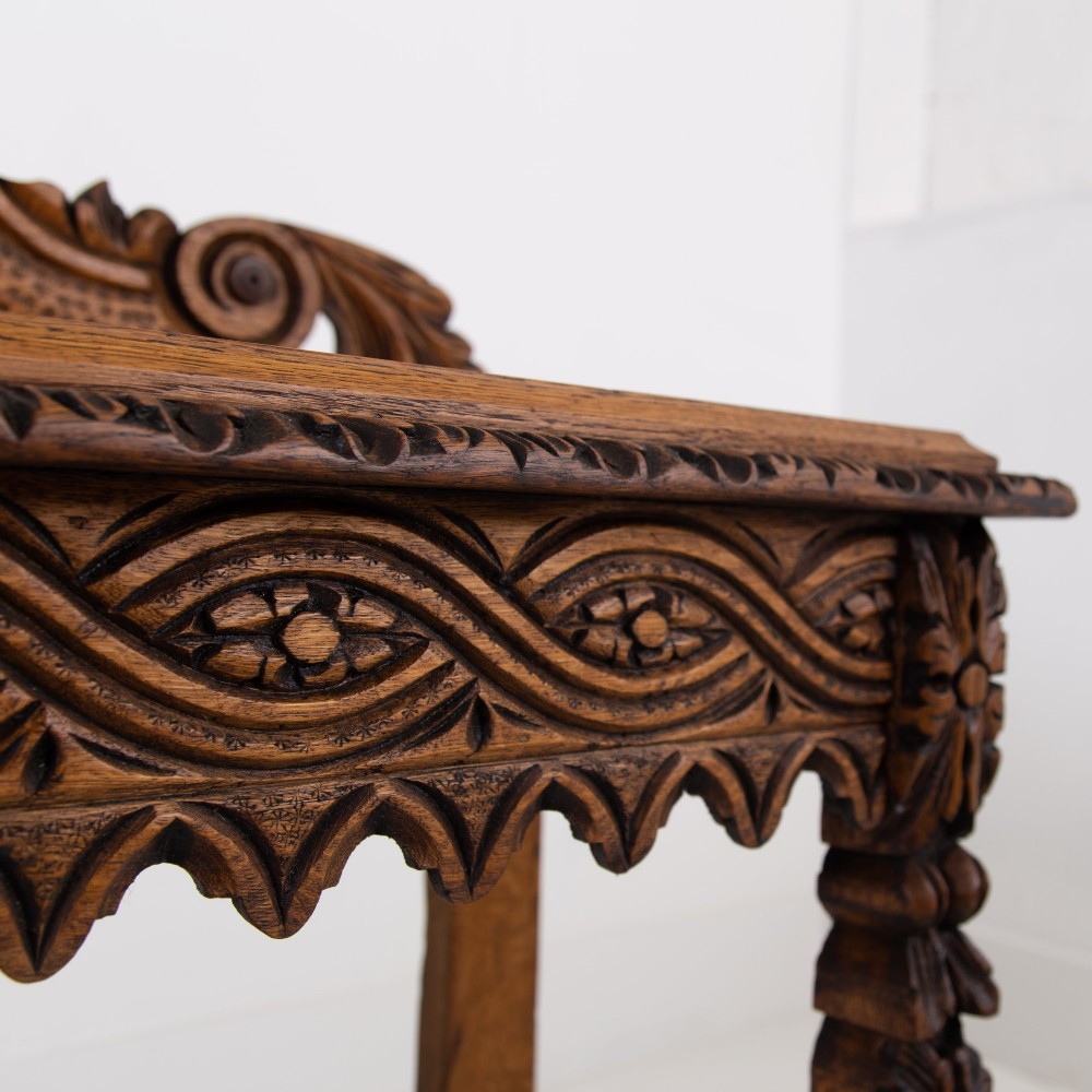 An ornate carved oak console table with a decorative mask crest upstand, an intricate interlace apron design, and carved turned legs. View VII