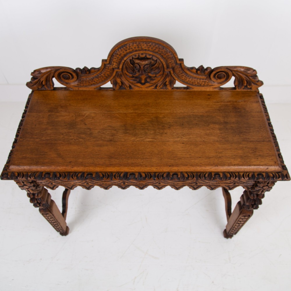 An ornate carved oak console table with a decorative mask crest upstand, an intricate interlace apron design, and carved turned legs. View XI