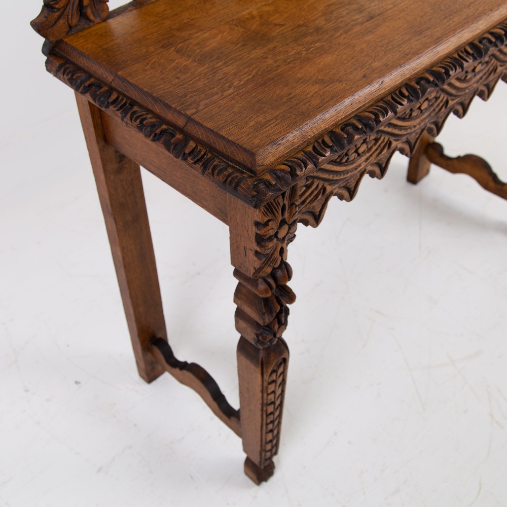 An ornate carved oak console table with a decorative mask crest upstand, an intricate interlace apron design, and carved turned legs. View XII