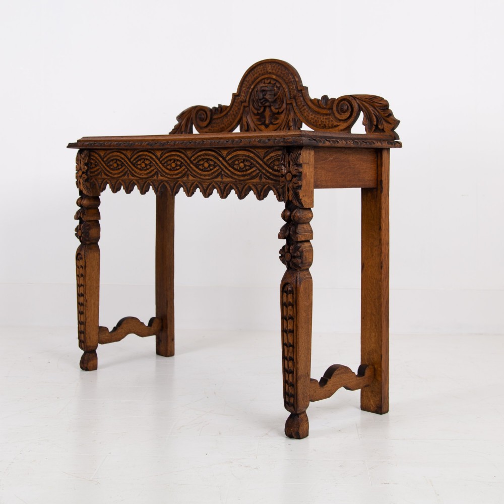 An ornate carved oak console table with a decorative mask crest upstand, an intricate interlace apron design, and carved turned legs. View XIV