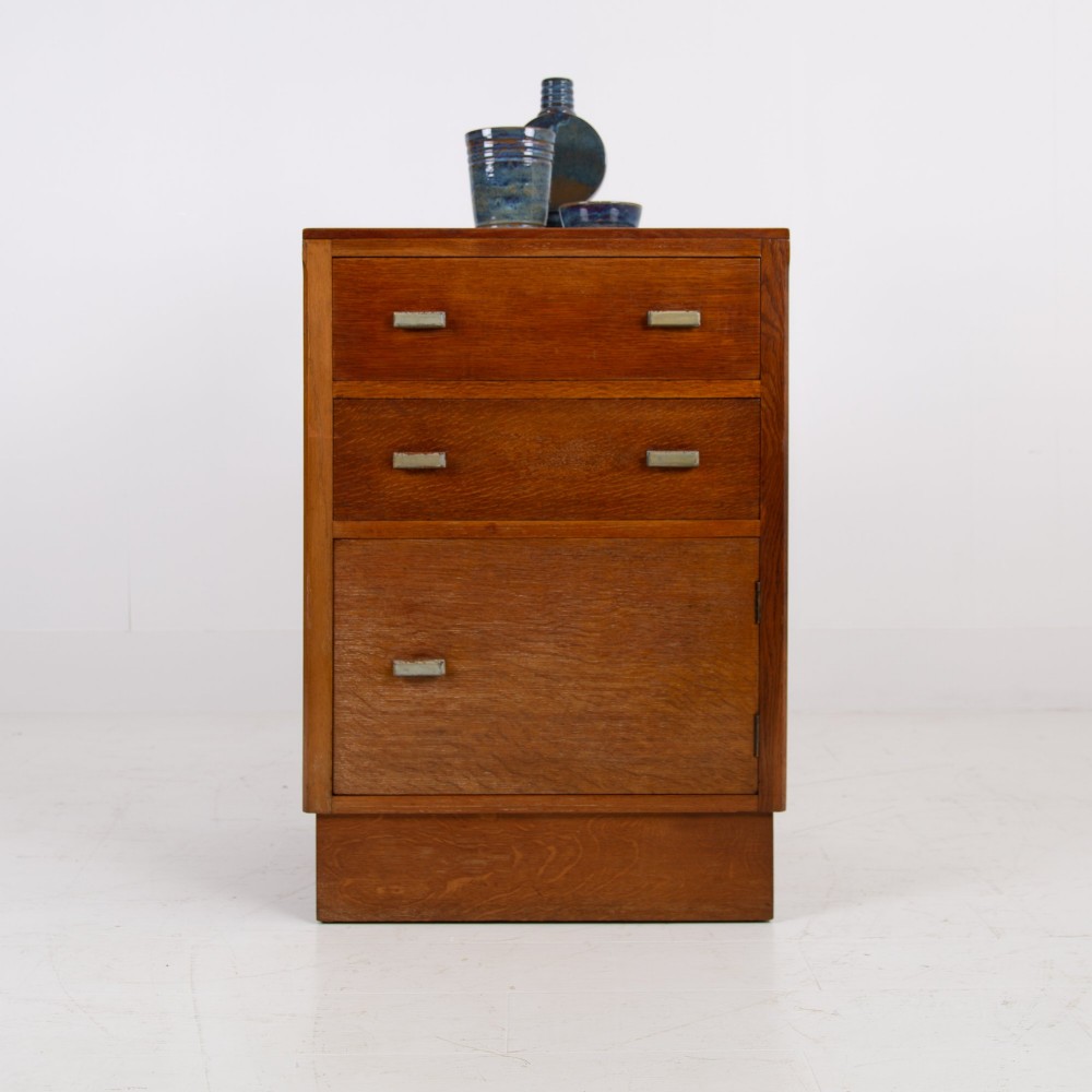 An Art Deco medium oak cabinet featuring two upper drawers, a lower cupboard door, and rectangular metal pulls on a plinth base.