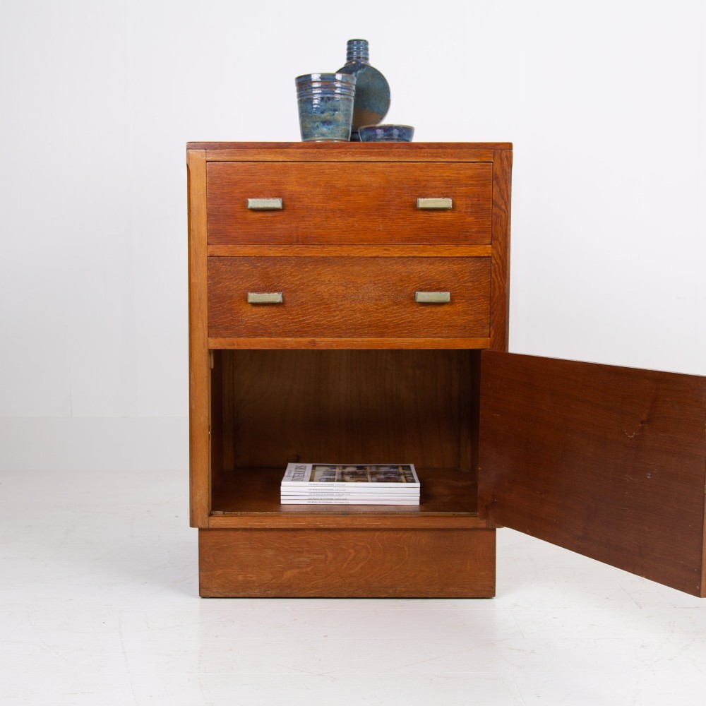 An Art Deco medium oak cabinet featuring two upper drawers, a lower cupboard door, and rectangular metal pulls on a plinth base. View II