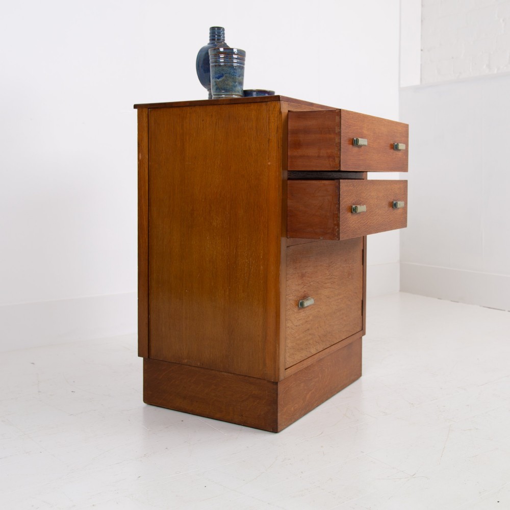 An Art Deco medium oak cabinet featuring two upper drawers, a lower cupboard door, and rectangular metal pulls on a plinth base. View III