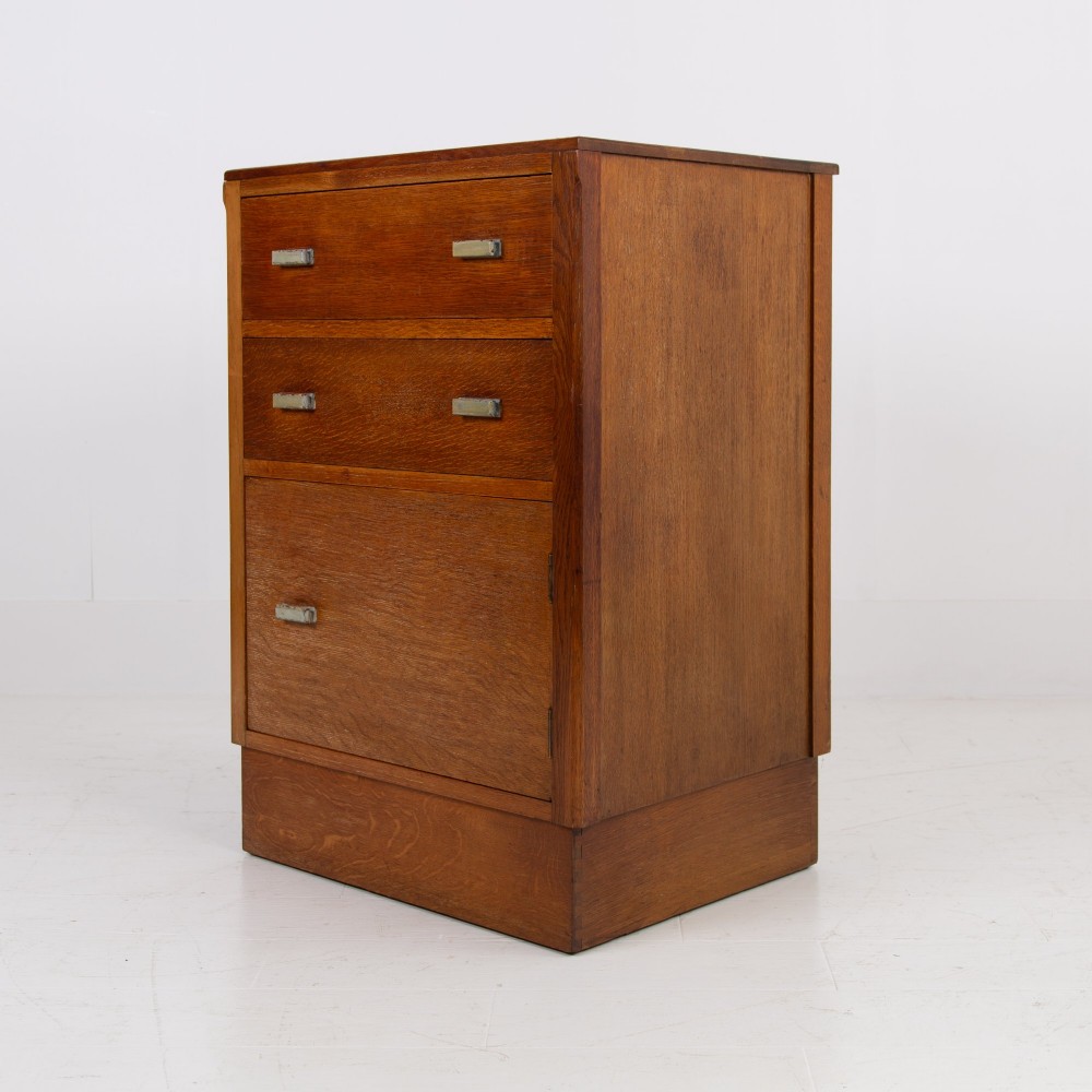 An Art Deco medium oak cabinet featuring two upper drawers, a lower cupboard door, and rectangular metal pulls on a plinth base. View IV
