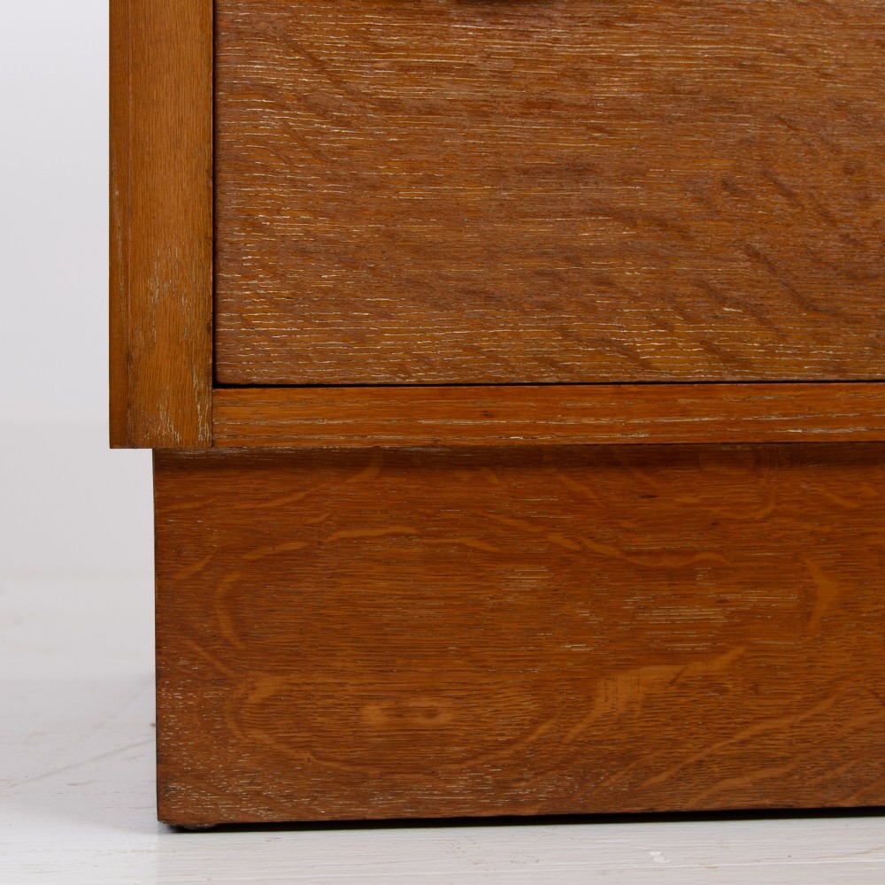 An Art Deco medium oak cabinet featuring two upper drawers, a lower cupboard door, and rectangular metal pulls on a plinth base. View VIII