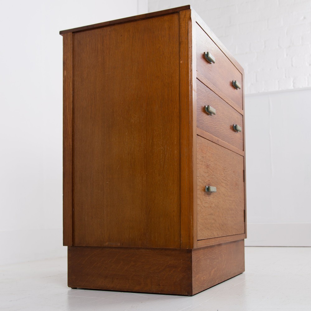 An Art Deco medium oak cabinet featuring two upper drawers, a lower cupboard door, and rectangular metal pulls on a plinth base. View IX