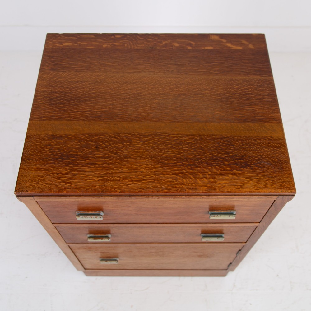 An Art Deco medium oak cabinet featuring two upper drawers, a lower cupboard door, and rectangular metal pulls on a plinth base. View XI