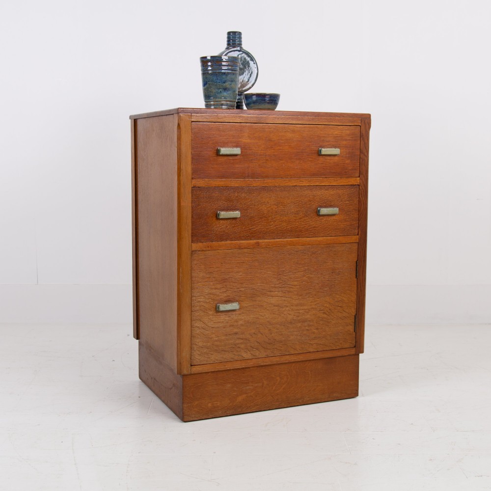 An Art Deco medium oak cabinet featuring two upper drawers, a lower cupboard door, and rectangular metal pulls on a plinth base. View XIII