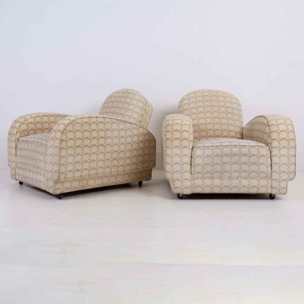 A pair of 1930s Art Deco upholstered armchairs featuring rounded arms, a scalloped fabric pattern, and small integrated casters.