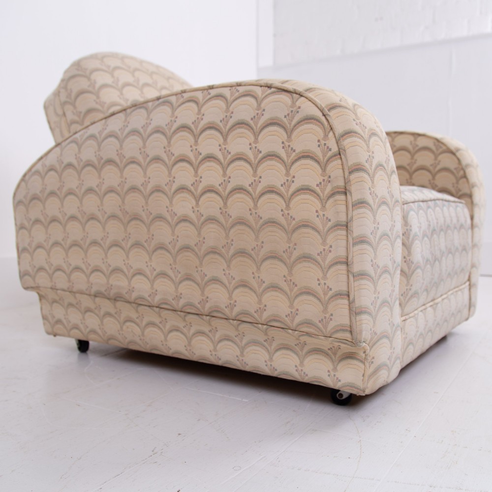 A pair of 1930s Art Deco upholstered armchairs featuring rounded arms, a scalloped fabric pattern, and small integrated casters. View V