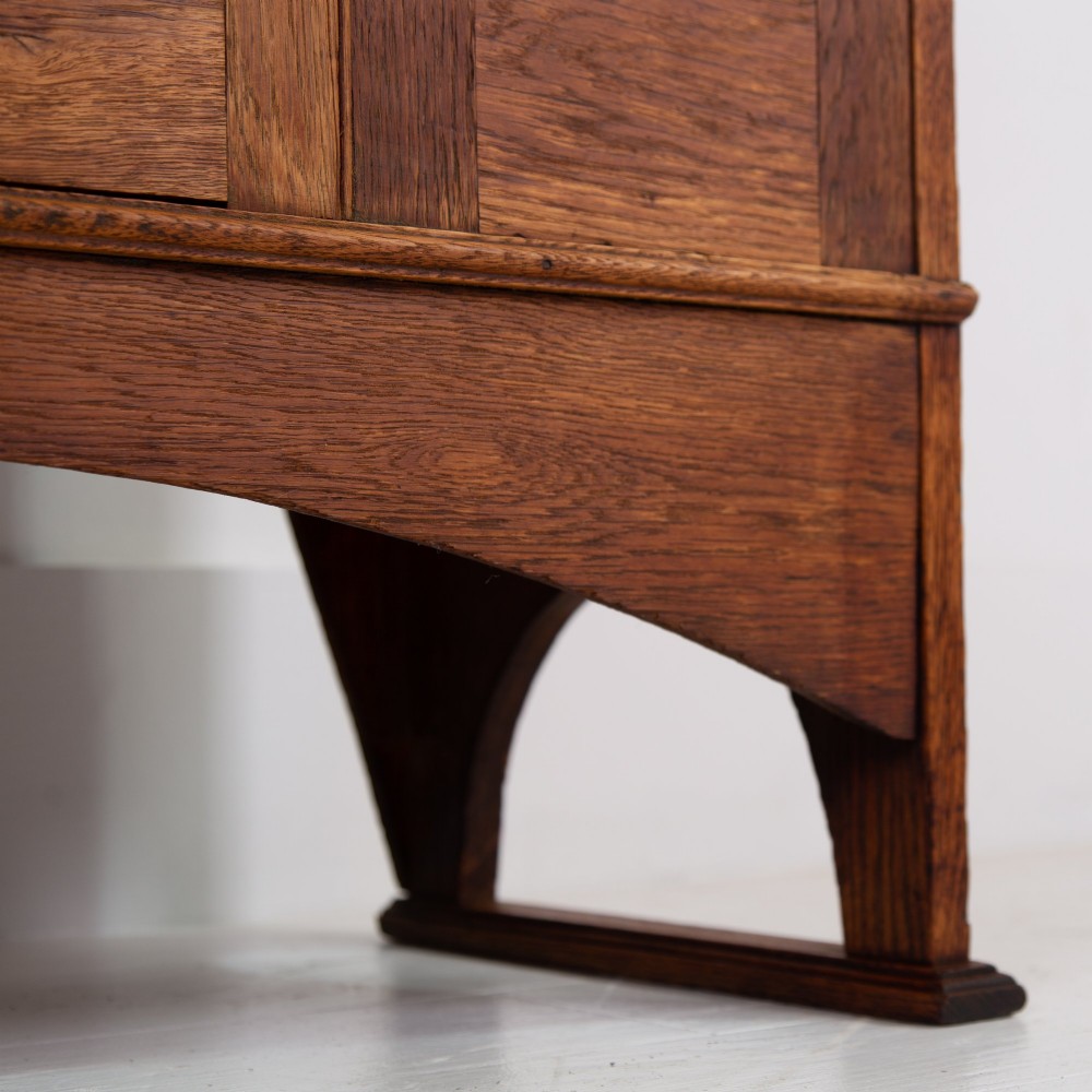 An Arts and Crafts oak hall wardrobe featuring a central mirrored door, dark glass roundel inserts near the top, and an arched apron base. View V