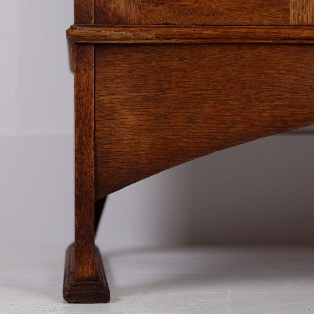 An Arts and Crafts oak hall wardrobe featuring a central mirrored door, dark glass roundel inserts near the top, and an arched apron base. View XIII