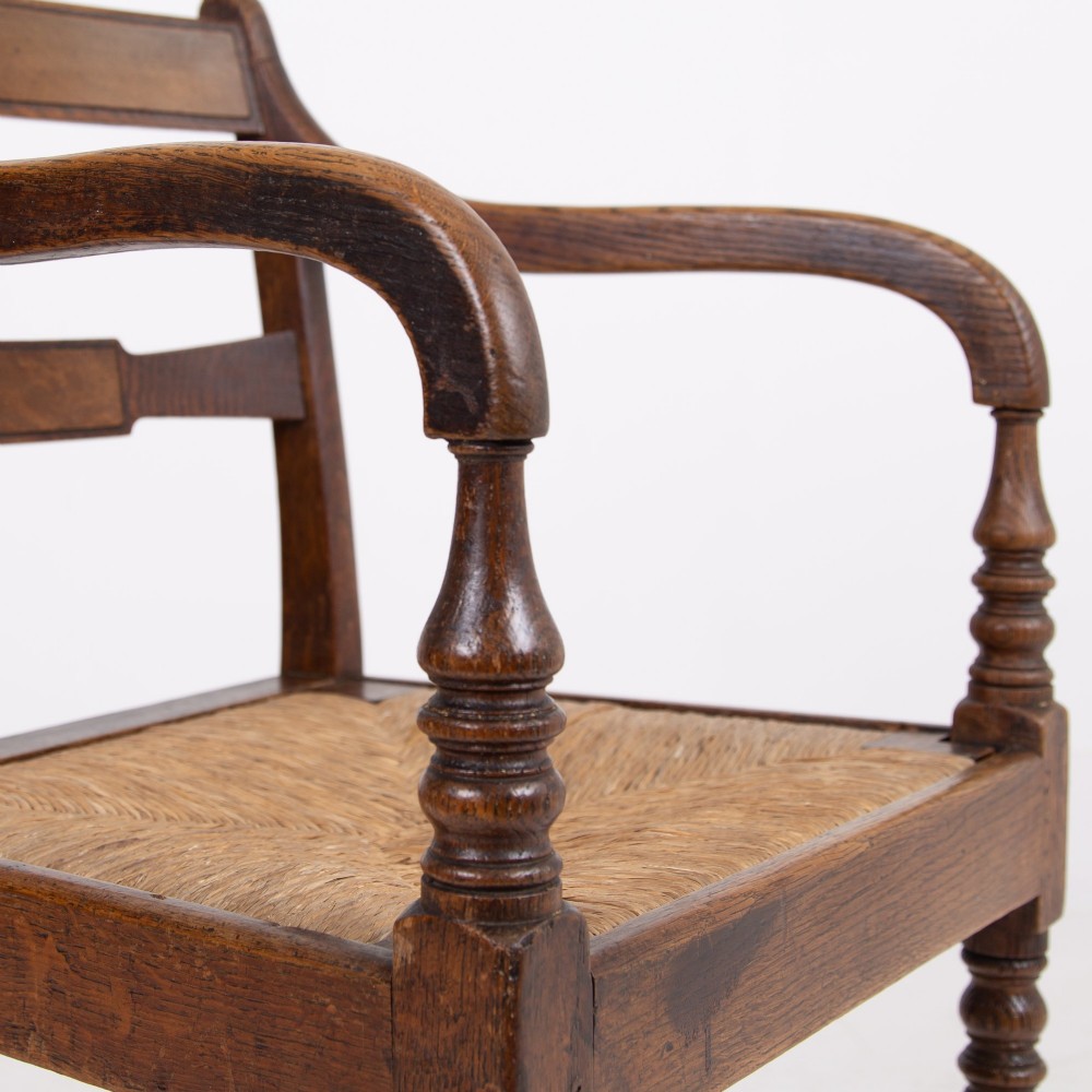 A pair of 1820s Georgian dark oak elbow chairs featuring woven rush seats, swept armrests, and turned front legs. View II
