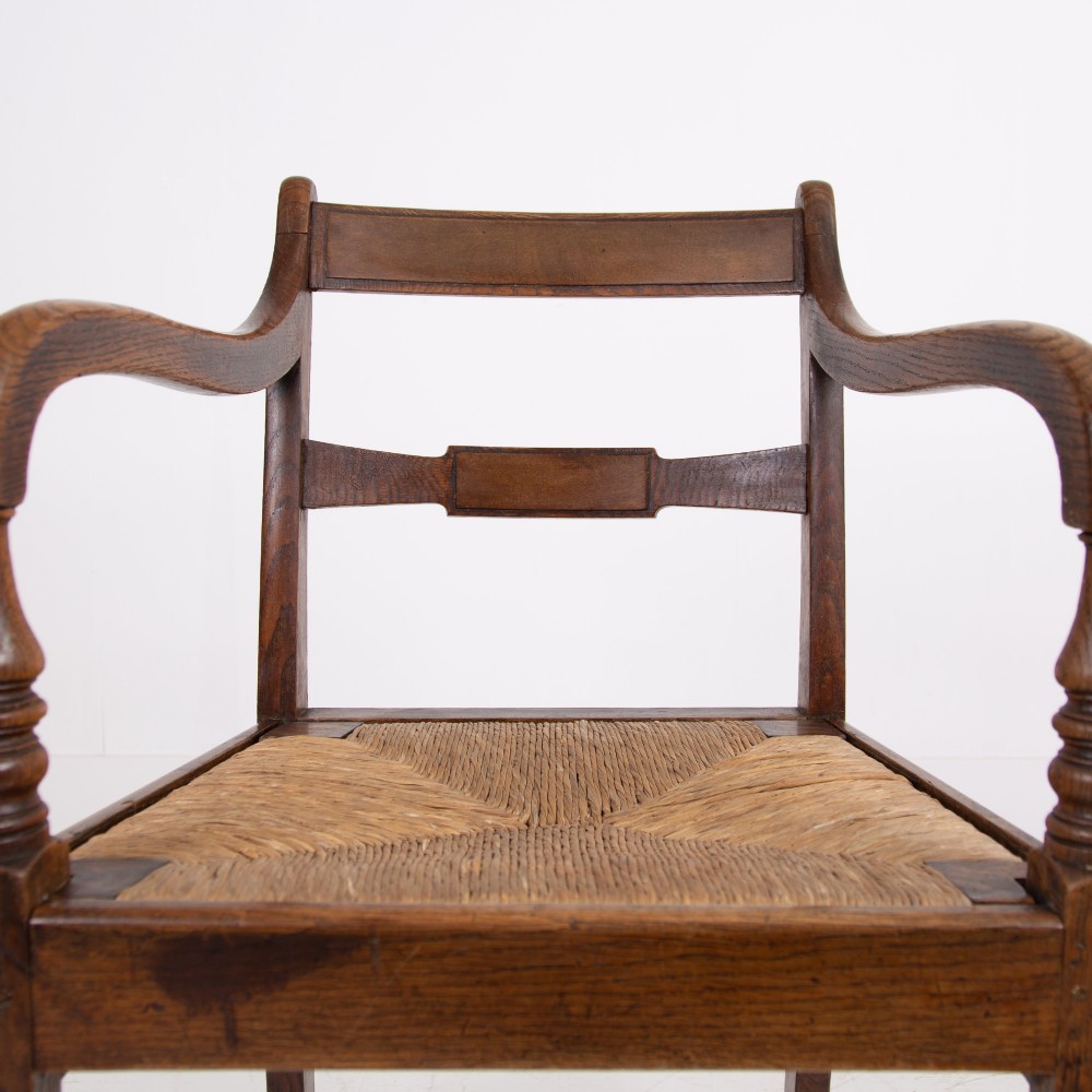 A pair of 1820s Georgian dark oak elbow chairs featuring woven rush seats, swept armrests, and turned front legs. View III