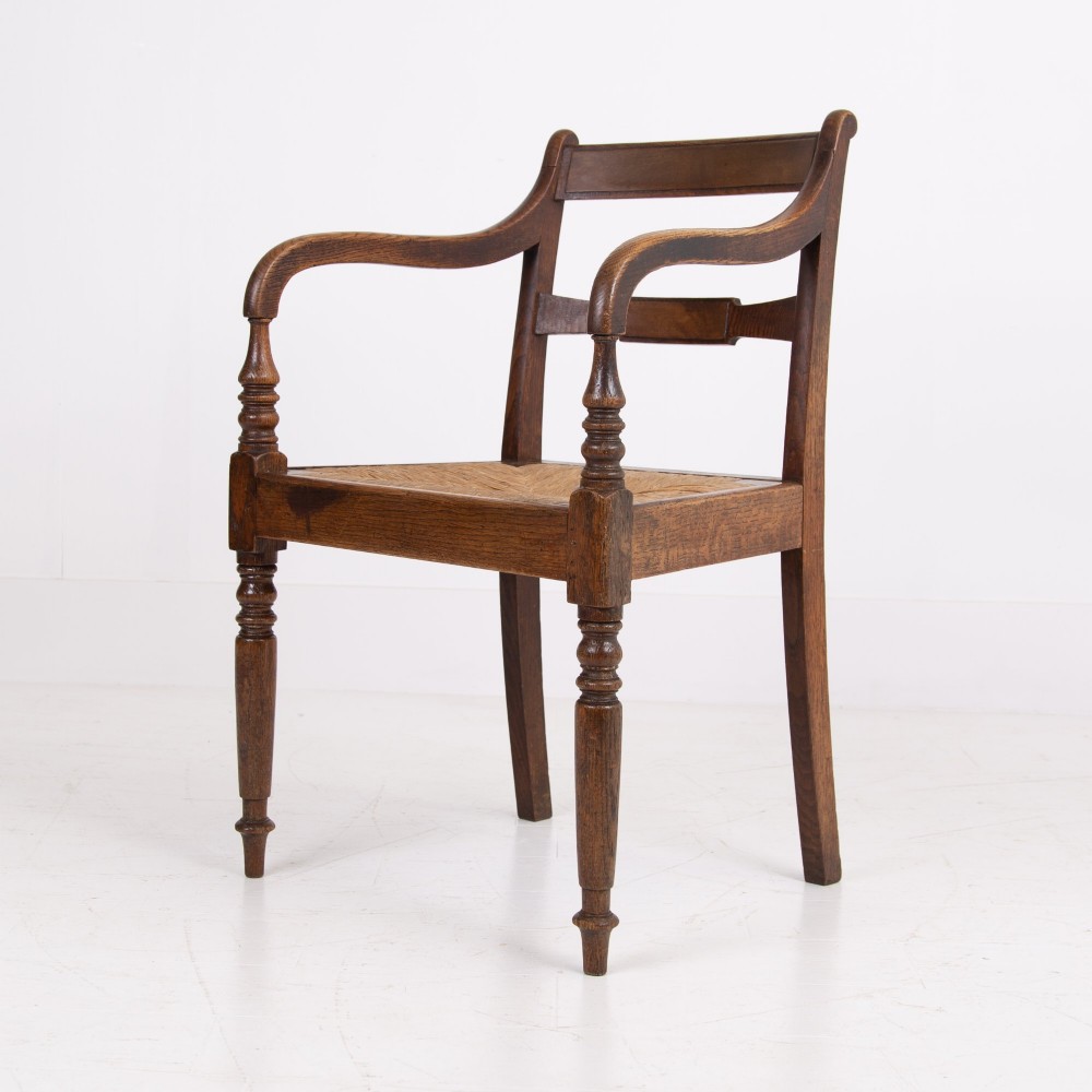A pair of 1820s Georgian dark oak elbow chairs featuring woven rush seats, swept armrests, and turned front legs. View IV