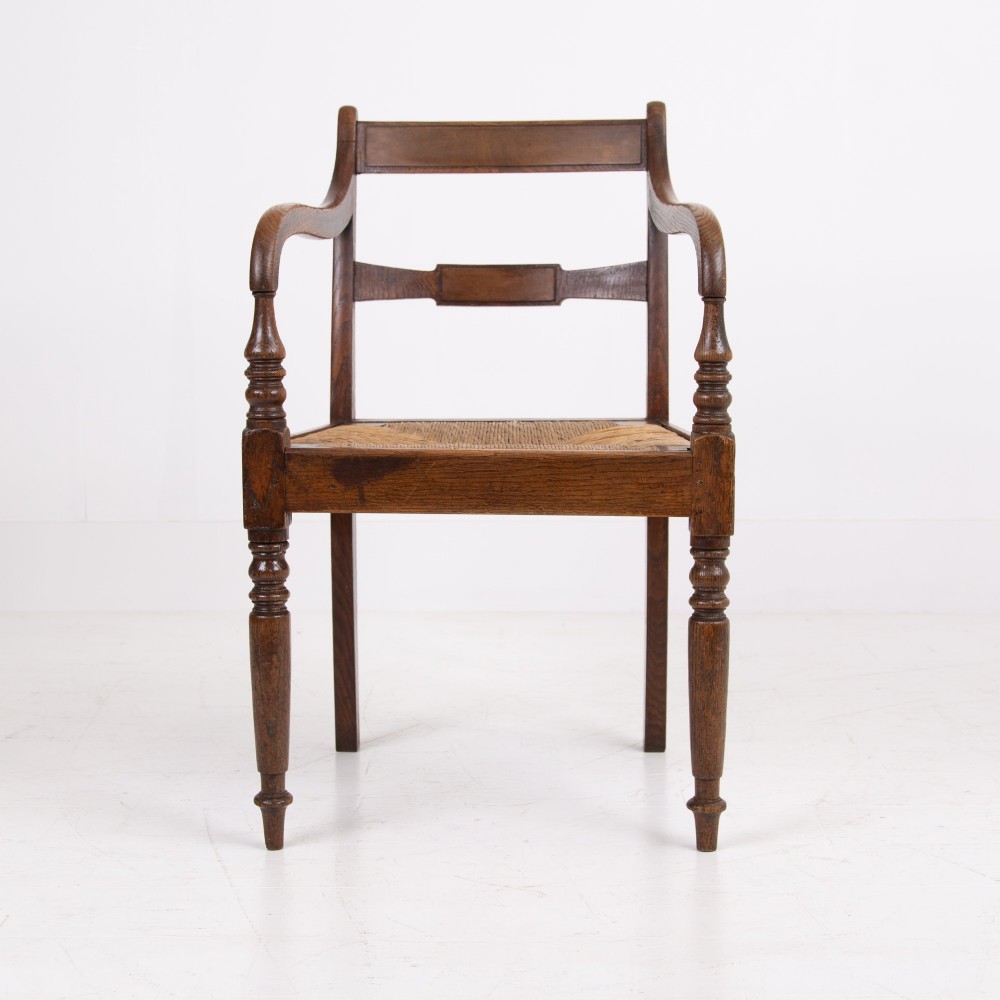 A pair of 1820s Georgian dark oak elbow chairs featuring woven rush seats, swept armrests, and turned front legs. View V