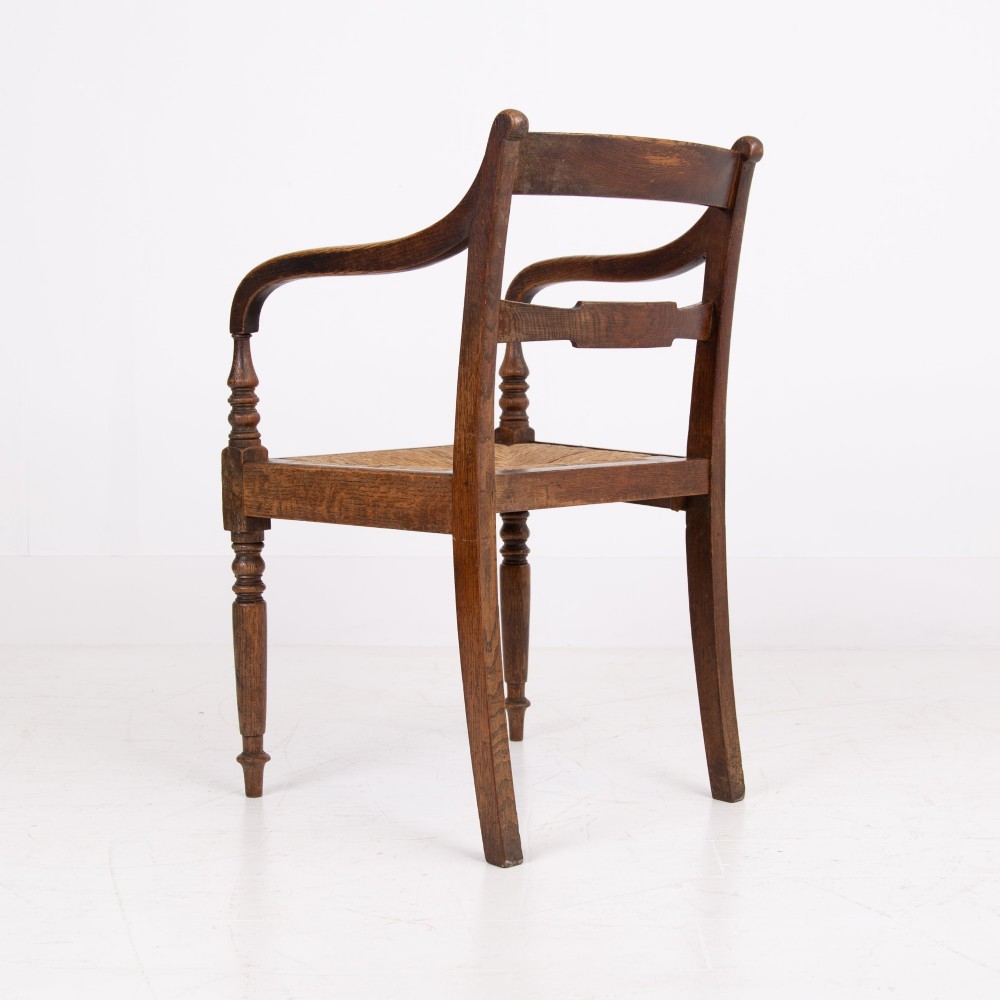 A pair of 1820s Georgian dark oak elbow chairs featuring woven rush seats, swept armrests, and turned front legs. View VI