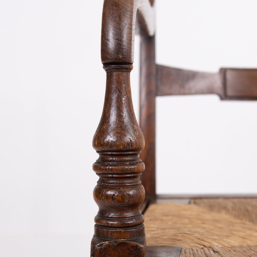 A pair of 1820s Georgian dark oak elbow chairs featuring woven rush seats, swept armrests, and turned front legs. View VII