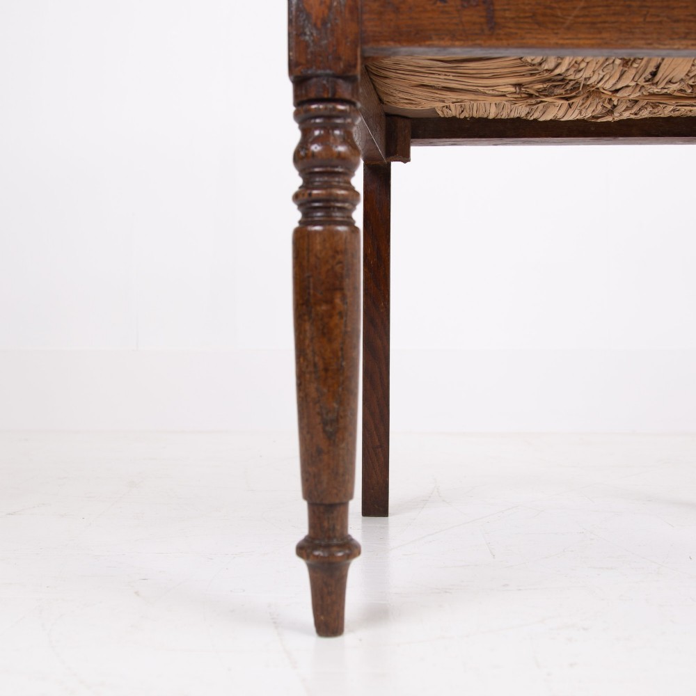 A pair of 1820s Georgian dark oak elbow chairs featuring woven rush seats, swept armrests, and turned front legs. View IX