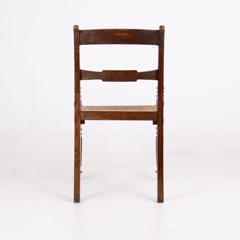 A pair of 1820s Georgian dark oak elbow chairs featuring woven rush seats, swept armrests, and turned front legs. View XIII