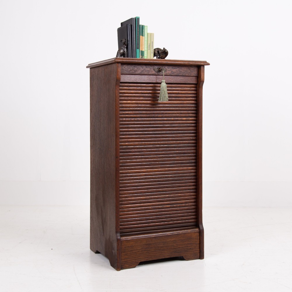 A tall dark oak filing cabinet with a vertical tambour slatted roller shutter door and brass lock plate.