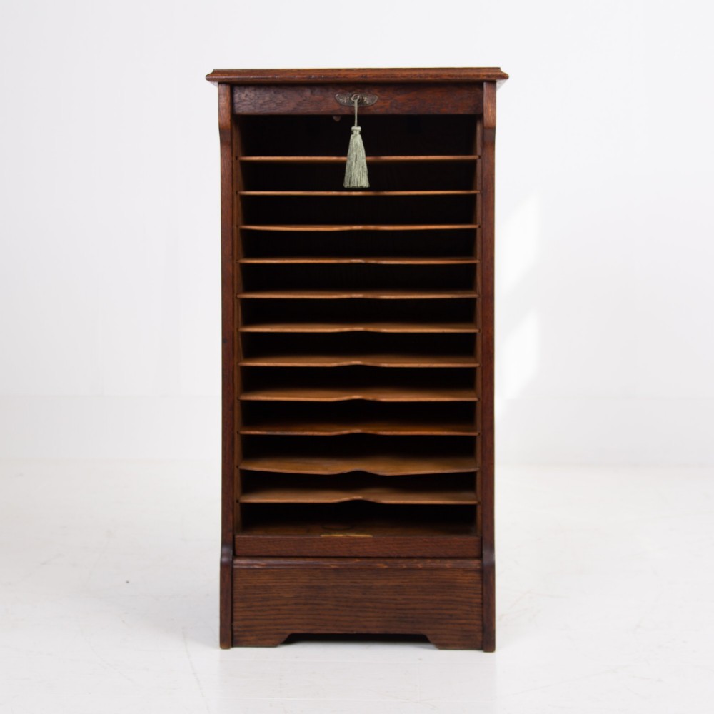 A tall dark oak filing cabinet with a vertical tambour slatted roller shutter door and brass lock plate. View III