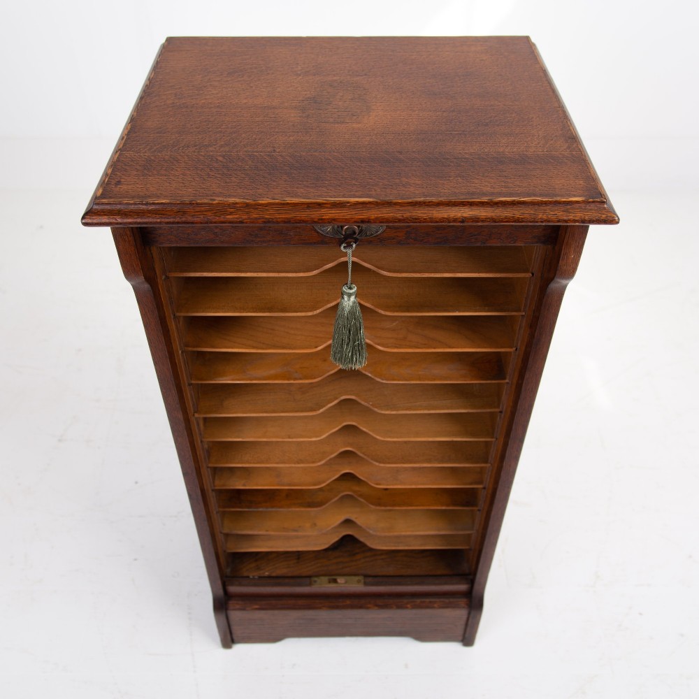 A tall dark oak filing cabinet with a vertical tambour slatted roller shutter door and brass lock plate. View IV