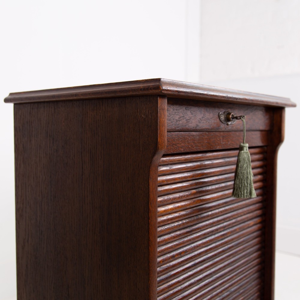A tall dark oak filing cabinet with a vertical tambour slatted roller shutter door and brass lock plate. View VI