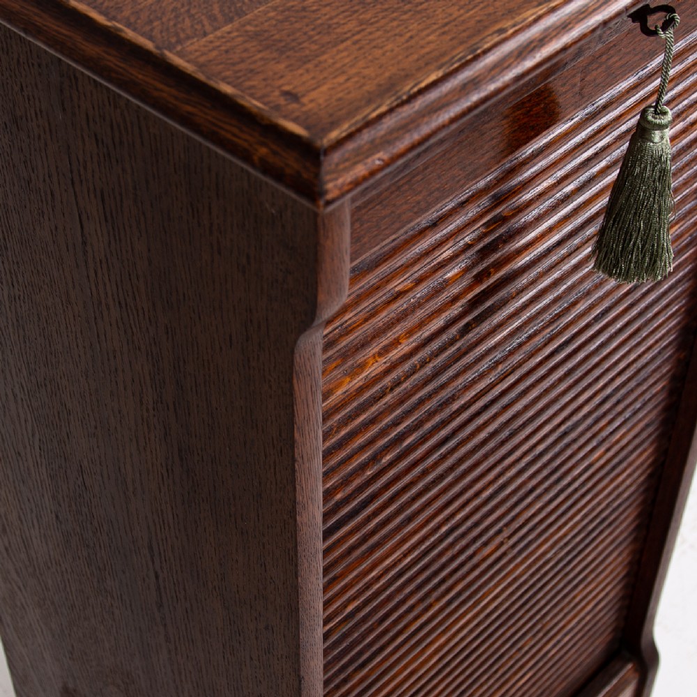 A tall dark oak filing cabinet with a vertical tambour slatted roller shutter door and brass lock plate. View VII