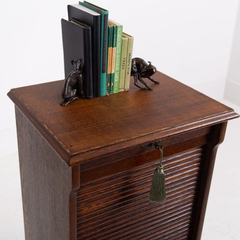 A tall dark oak filing cabinet with a vertical tambour slatted roller shutter door and brass lock plate. View VIII