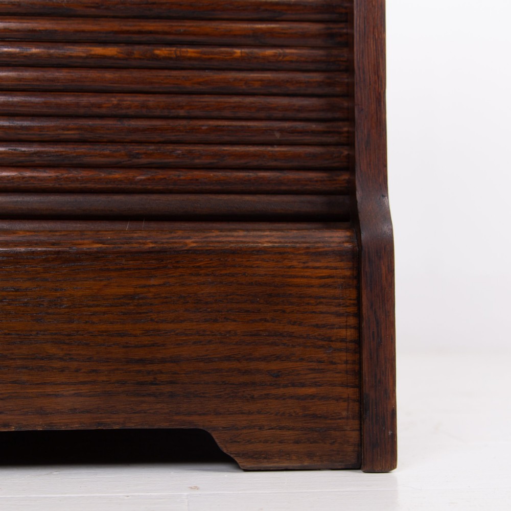 A tall dark oak filing cabinet with a vertical tambour slatted roller shutter door and brass lock plate. View X