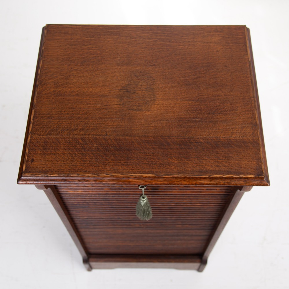 A tall dark oak filing cabinet with a vertical tambour slatted roller shutter door and brass lock plate. View XI