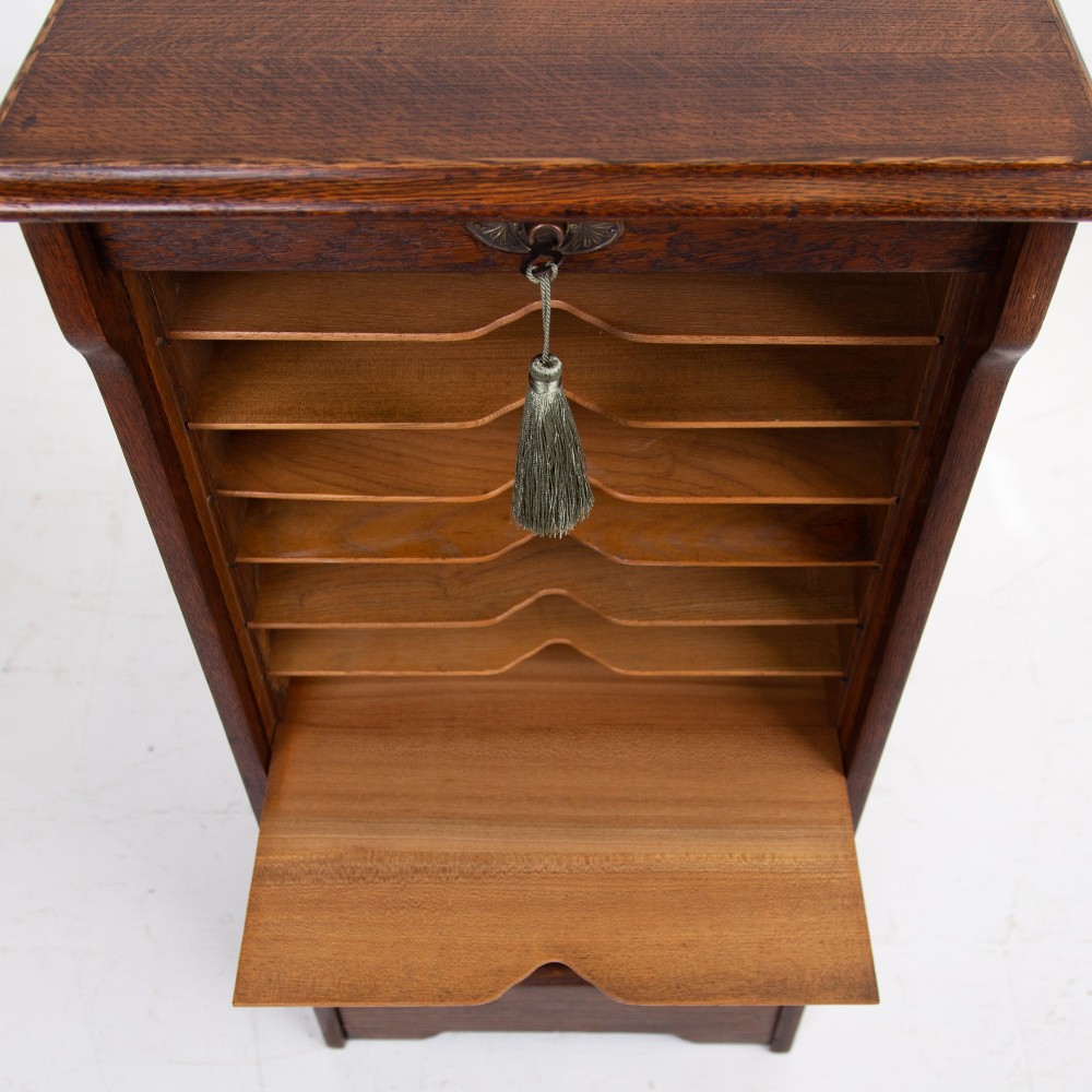 A tall dark oak filing cabinet with a vertical tambour slatted roller shutter door and brass lock plate. View XII