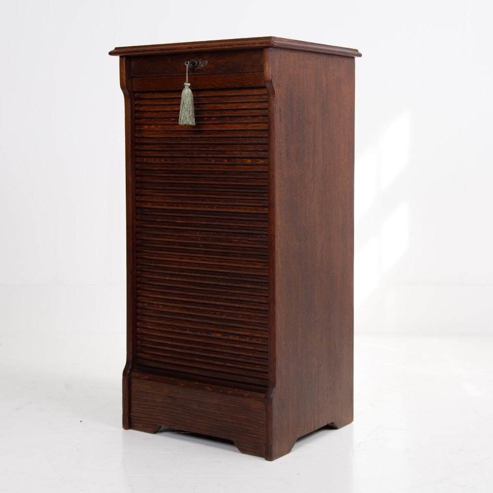 A tall dark oak filing cabinet with a vertical tambour slatted roller shutter door and brass lock plate. View XIII